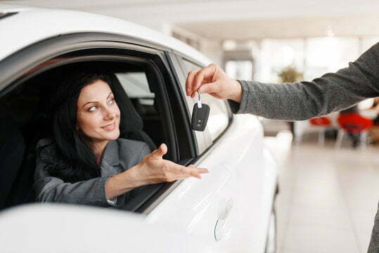Happy woman takes the key to new car in showroom